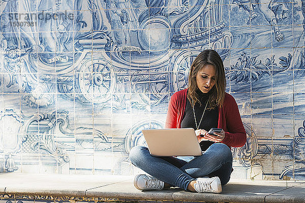 Frau mit Laptop und Smartphone vor Mosaikwand