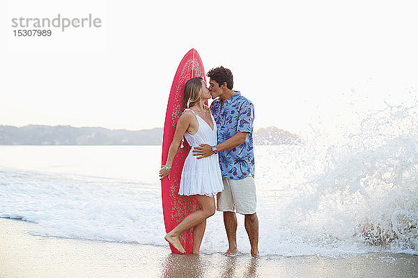 Verliebtes Paar mit Surfbrett küsst sich am Strand  Sayulita  Nayarit  Mexiko
