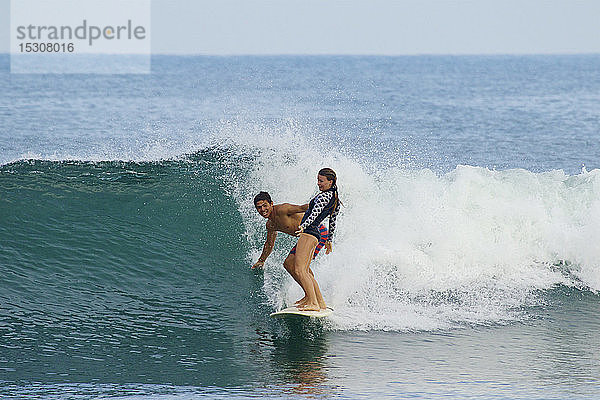 Junges Paar teilt sich ein Surfbrett und surft auf einer Meereswelle