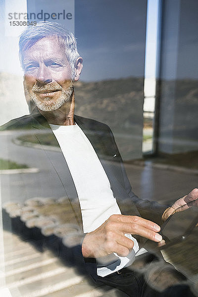 Lächelnder Senior-Geschäftsmann mit Tablette am Fenster