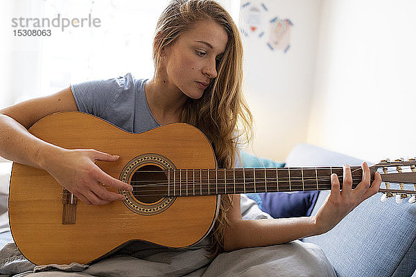 Junge Frau spielt zu Hause Gitarre mit beschädigter Saite
