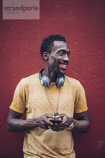 Porträt eines lächelnden Mannes mit Kopfhörer und Smartphone