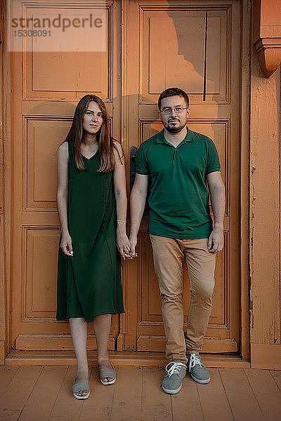 Porträt eines Paares  das bei Sonnenuntergang Hand in Hand vor einer Holztür steht