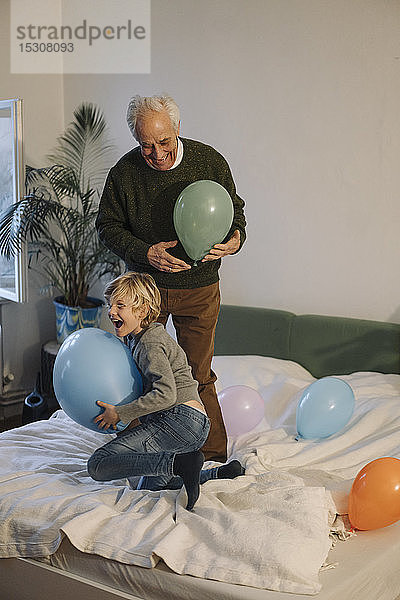 Glücklicher Großvater und Enkel spielen zu Hause mit Luftballons auf dem Bett