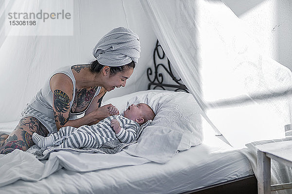 Tätowierte junge Frau mit ihrem Baby im Himmelbett