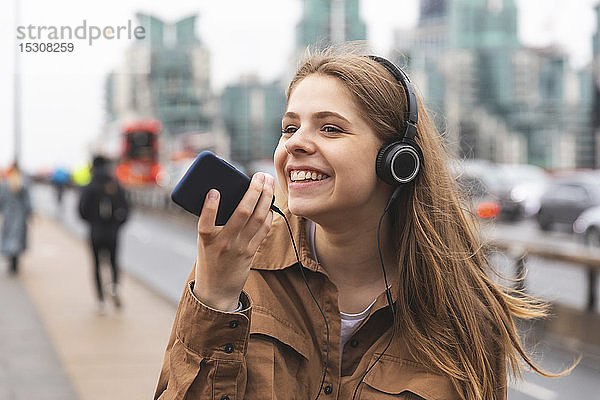 Glückliche junge Frau mit Kopfhörern und Handy in der Stadt  London  UK