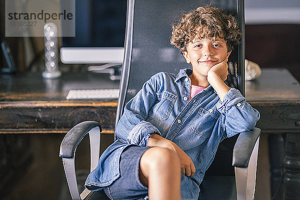 Porträt eines lächelnden Jungen  der auf einem Bürostuhl sitzt