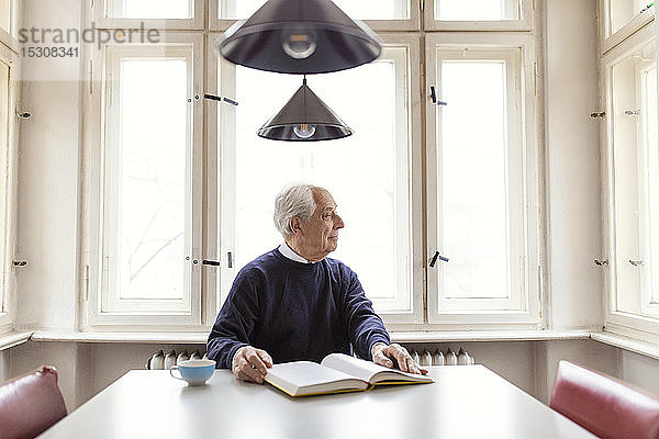 Älterer Mann liest Buch bei Tisch zu Hause