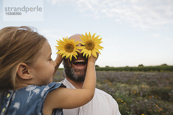 Tochter bedeckt Augen des Vaters mit Sonnenblumen