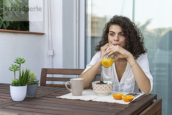 Junge Frau trinkt Orangensaft auf dem Balkon