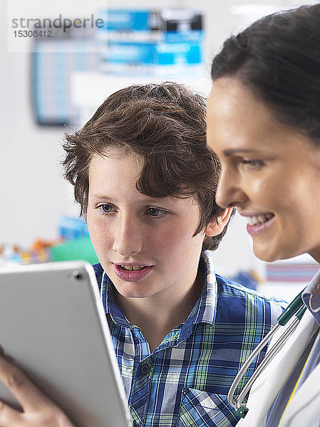 Ärztin zeigt einem jungen männlichen Patienten seine Laborergebnisse auf einem digitalen Tablett in der Klinik