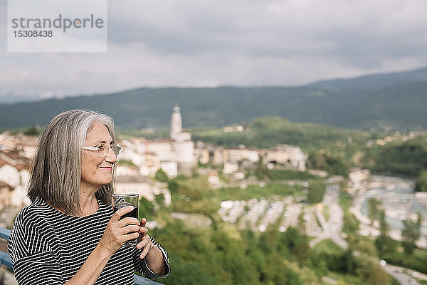 Entspannte ältere Frau mit einem Glas Kaffee auf ihrer Dachterrasse  Belluno  Italien