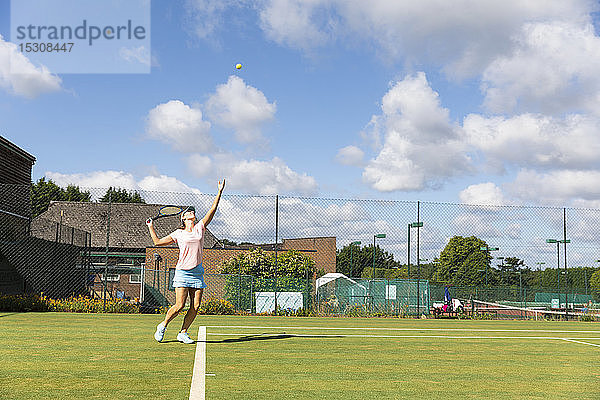 Reife Frau serviert während eines Tennisspiels auf Rasen
