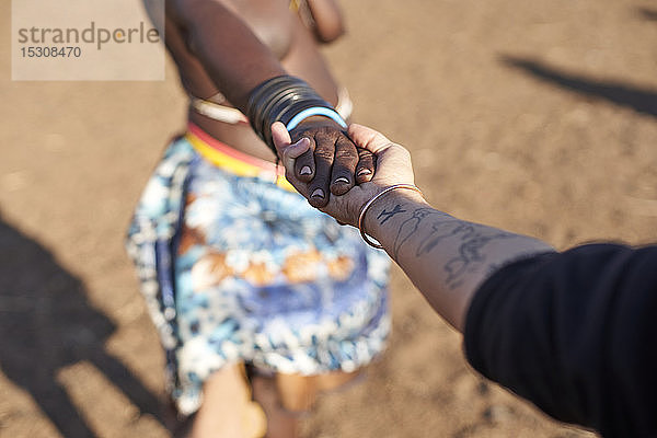 Traditionelle Muhacaona-Frau und weiße Frau halten Händchen  Oncocua  Angola