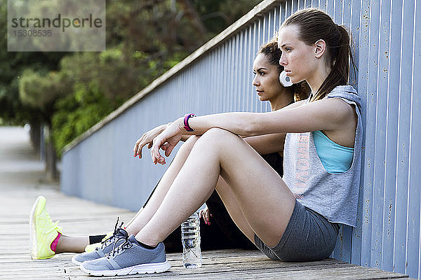 Zwei sportliche junge Frauen entspannen sich nach dem Training auf einer Brücke