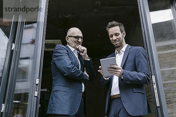 Lächelnder älterer und mittel-erwachsener Geschäftsmann mit Tablette bei einer Besprechung