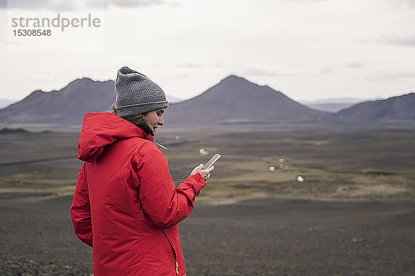 Junge Frau mit Smartphone im isländischen Hochland