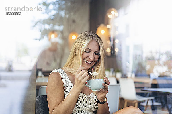 Porträt einer glücklichen blonden Frau  die in einem Cafe Cappuccino trinkt