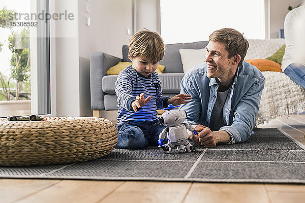 Vater und Sohn liegen auf dem Boden und spielen mit einem Spielzeugroboter