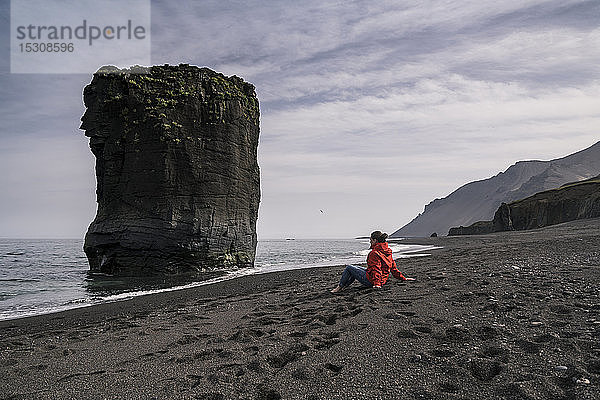 Frau am Lavastrand im Südosten Islands mit Blick auf das Meer