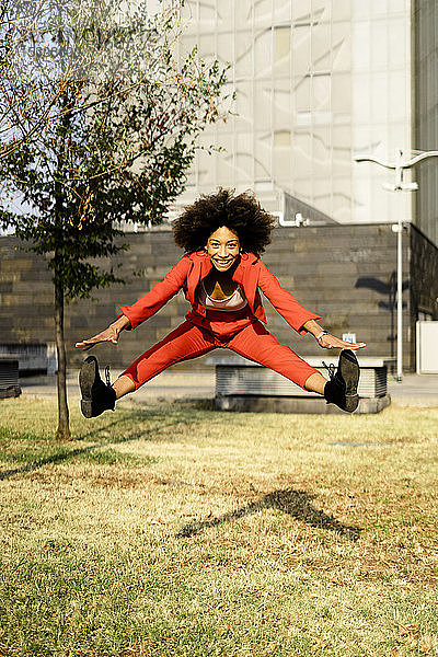 Porträt einer glücklichen jungen Frau in modischem roten Hosenanzug  die in die Luft springt