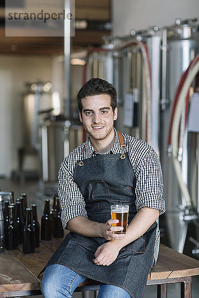 Porträt eines lächelnden jungen Mannes  der in einer Brauerei ein Bier trinkt