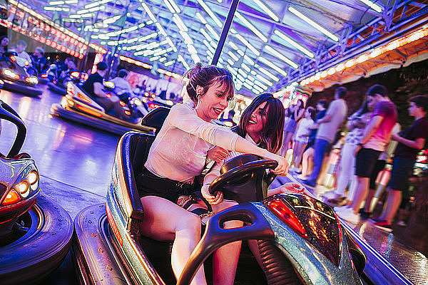 Zwei junge Frauen fahren nachts in einem Autoscooter auf einem Rummelplatz