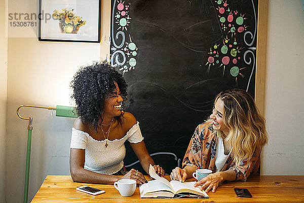 Multikulturelle Frauen  die in einem Café lachen und ein Buch lesen