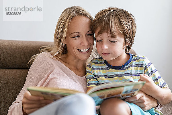 Mutter und Sohn lesen zu Hause auf der Couch gemeinsam ein Buch