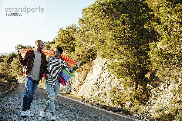 Homosexuelles Paar mit der Fahne Gay Pride geht auf einer Straße in den Bergen