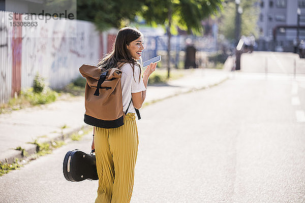 Junge Frau trägt Geigenkoffer mit Handy auf der Strasse