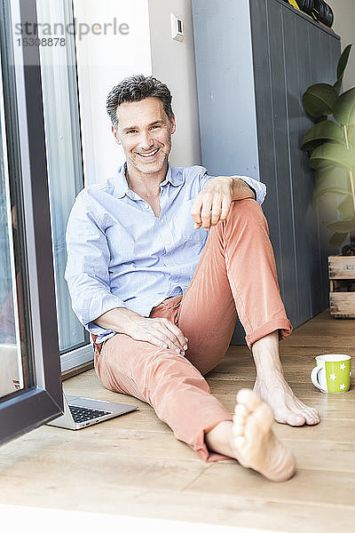 Reifer Mann entspannt sich zu Hause bei einer Tasse Kaffee  mit Laptop