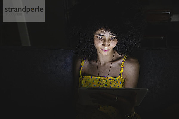 Junge Frau benutzt ihr digitales Tablet in der Nacht auf dem Sofa