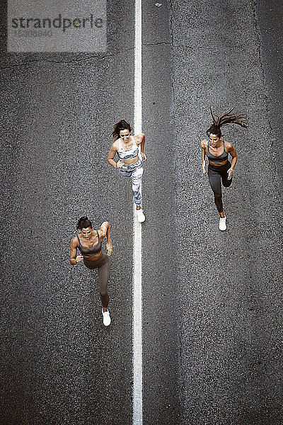 Draufsicht auf drei sportliche junge Frauen  die auf einer Straße laufen