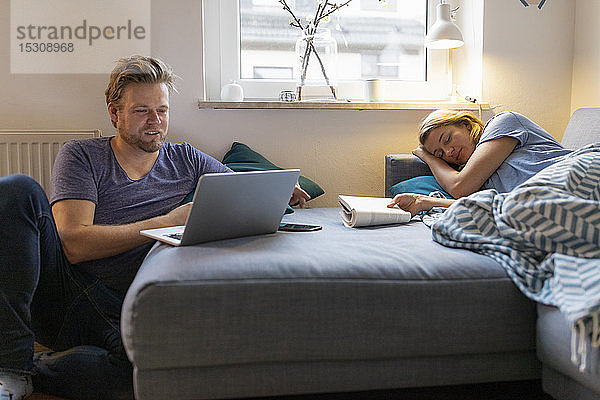 Junge Frau  die zu Hause mit ihrem Partner auf der Couch liegt und einen Laptop benutzt