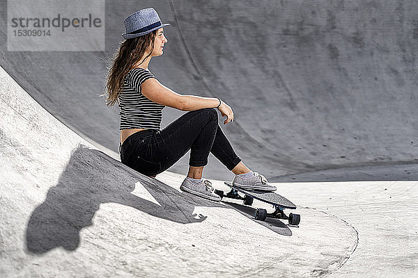 Junge Frau mit Skateboard im Skatepark sitzend