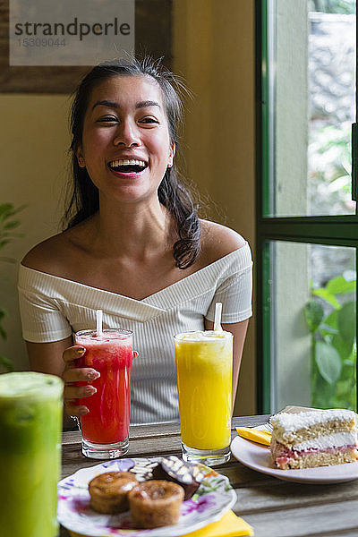 Lachende junge Frau trinkt einen Smoothie in einem Café