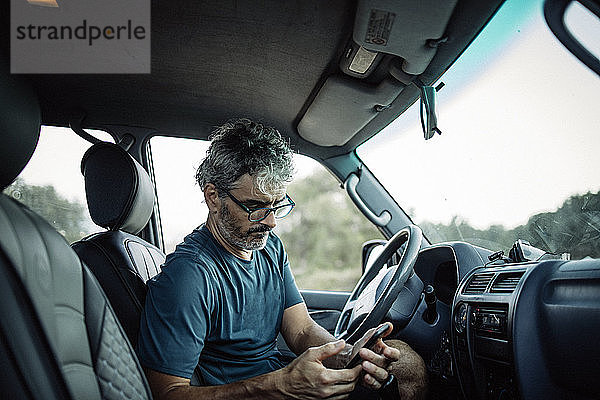 Reifer Mann sitzt in seinem Geländewagen und checkt sein Smartphone
