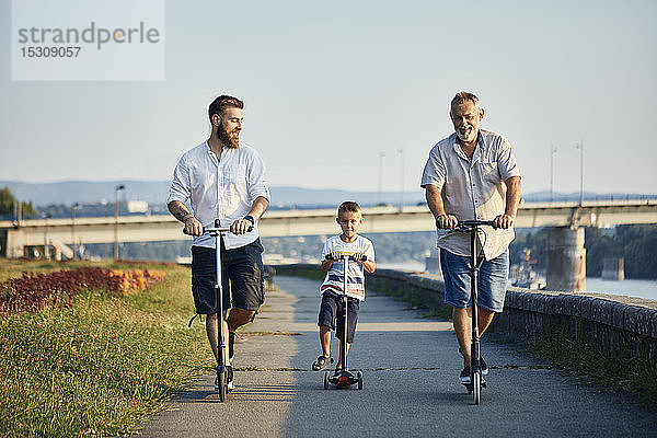 Großvater  Vater und Sohn fahren Roller am Flussufer
