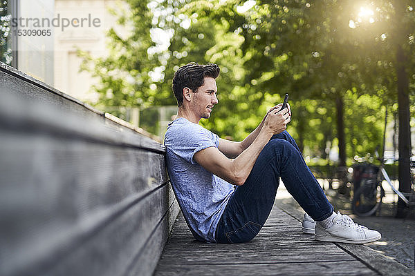 Mann sitzt auf Bank mit Smartphone