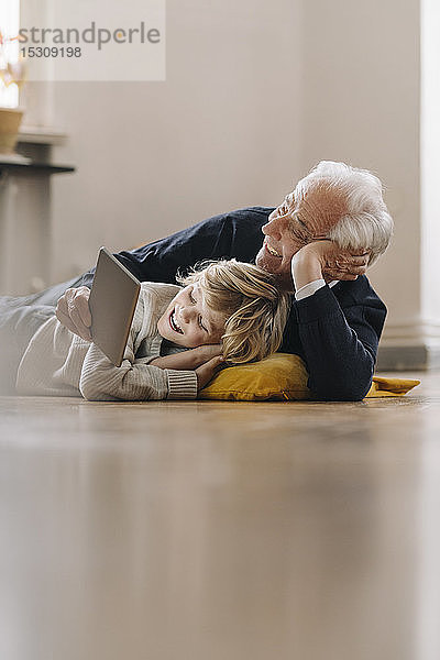 Glücklicher Großvater und Enkel  die zu Hause mit einer Tablette auf dem Boden liegen