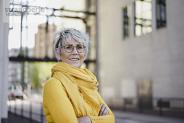 Bildnis einer reifen Frau mit grauen Haaren  die eine Brille trägt und gelb gekleidet ist