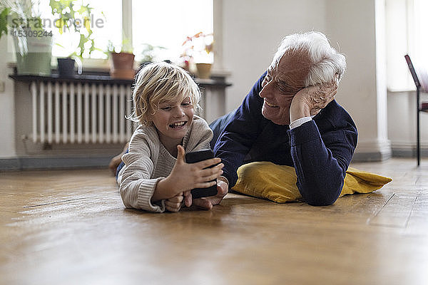 Großvater und Enkel liegen zu Hause auf dem Boden und benutzen ein Smartphone