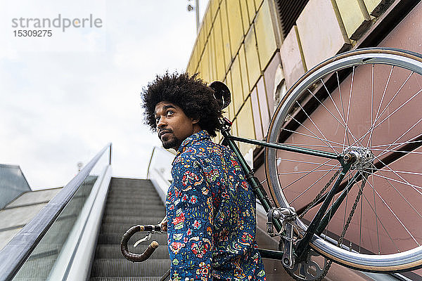 Eleganter Mann trägt Fahrrad auf Rolltreppe