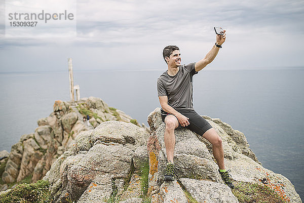 Trailrunner sitzt auf einem Felsen in der Küstenlandschaft und nimmt ein Selfie  Ferrol  Spanien