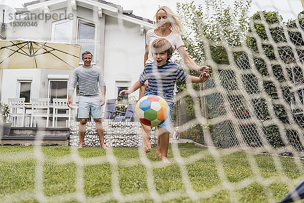 Glückliche Familie spielt Fussball im Garten