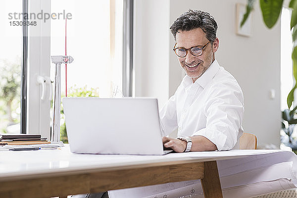 Geschäftsmann im Büro sitzen  Laptop benutzen  Modell eines Windrads betrachten