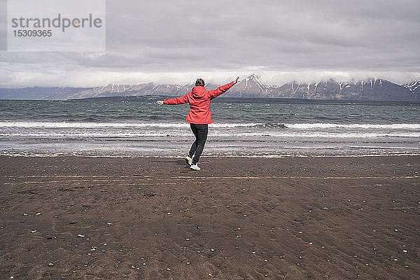 Junge Frau tanzt am Lavastrand am Eyjafjordur-Fjord  Island