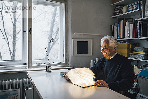Älterer Mann mit leuchtendem Buch auf dem Tisch zu Hause