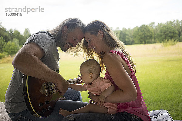 Vater  Mutter und kleines Mädchen sitzen mit Gitarre im Freien